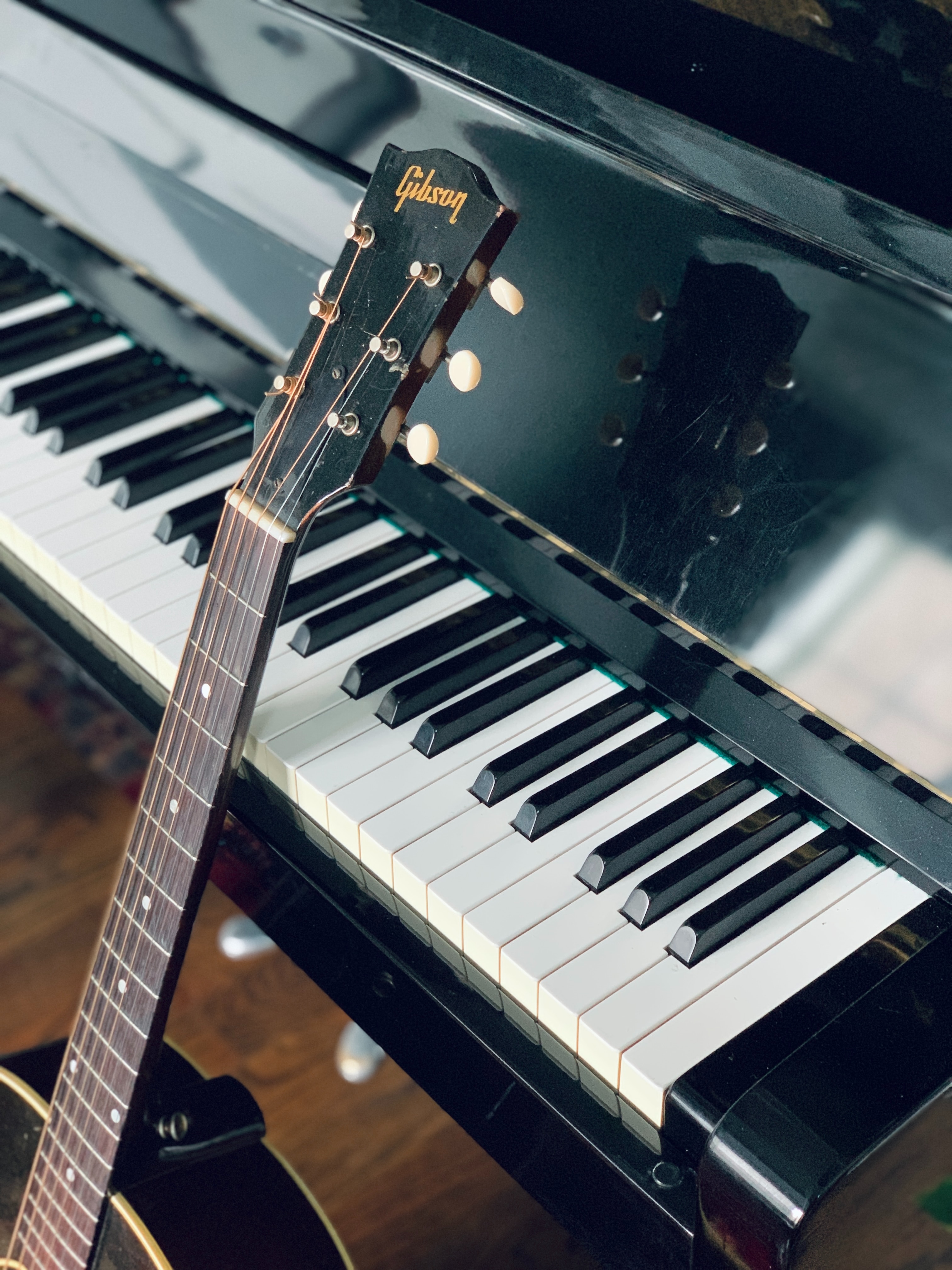 acoustic Gibson guitar by the piano